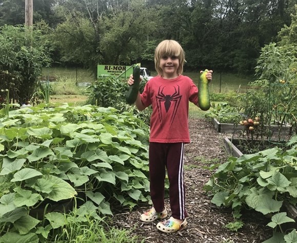 Alex, gardener Olive Mitchell’s young gardening companion, shows off some of their harvest from a raised bed in MUBG’s Henry Kirklin Community Garden.,